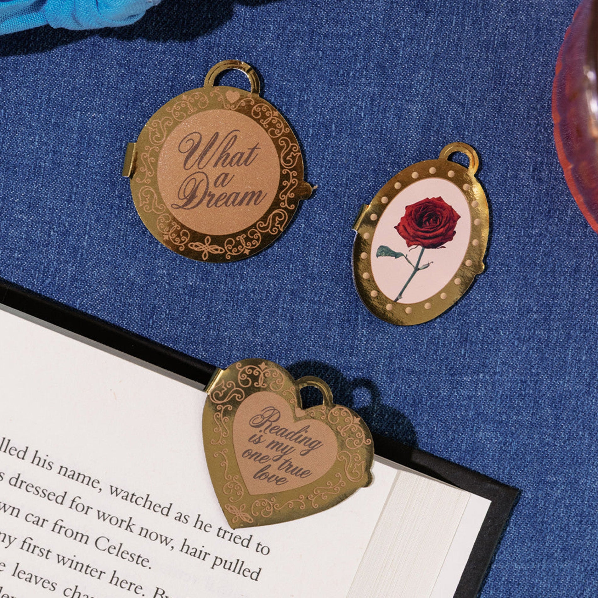 Three decorative bookmarks with engraved text and a rose on a blue fabric background.
