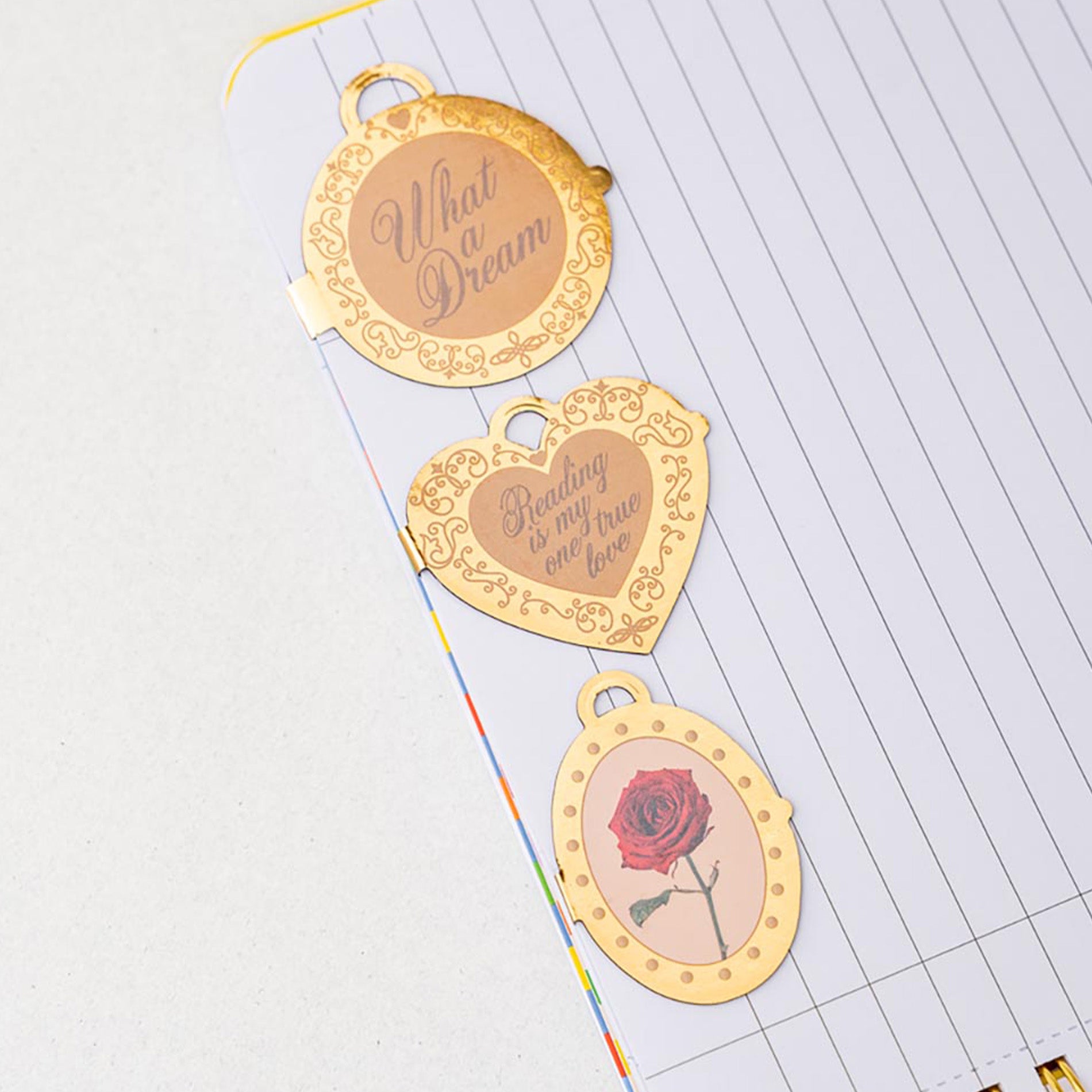 Three gold bookmarks with engraved text and a rose design on a lined paper background.