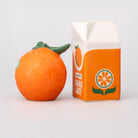 Orange fruit next to a carton of orange juice on a light gray background