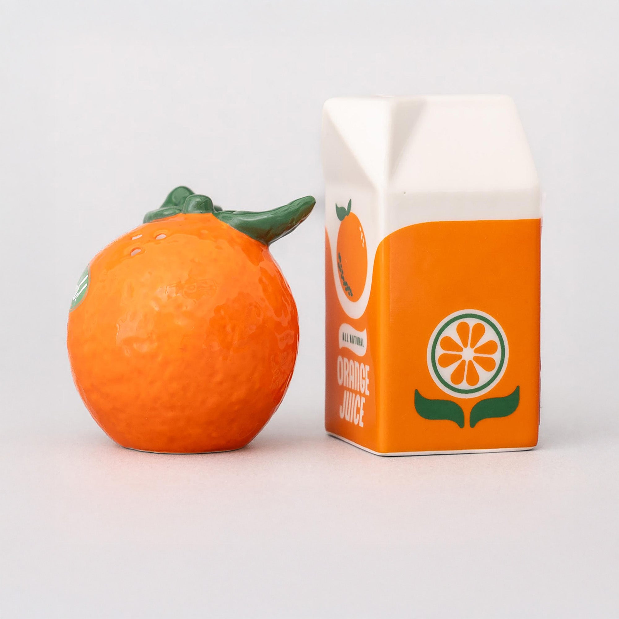 Orange fruit next to a carton of orange juice on a light gray background