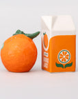 Orange fruit next to a carton of orange juice on a light gray background