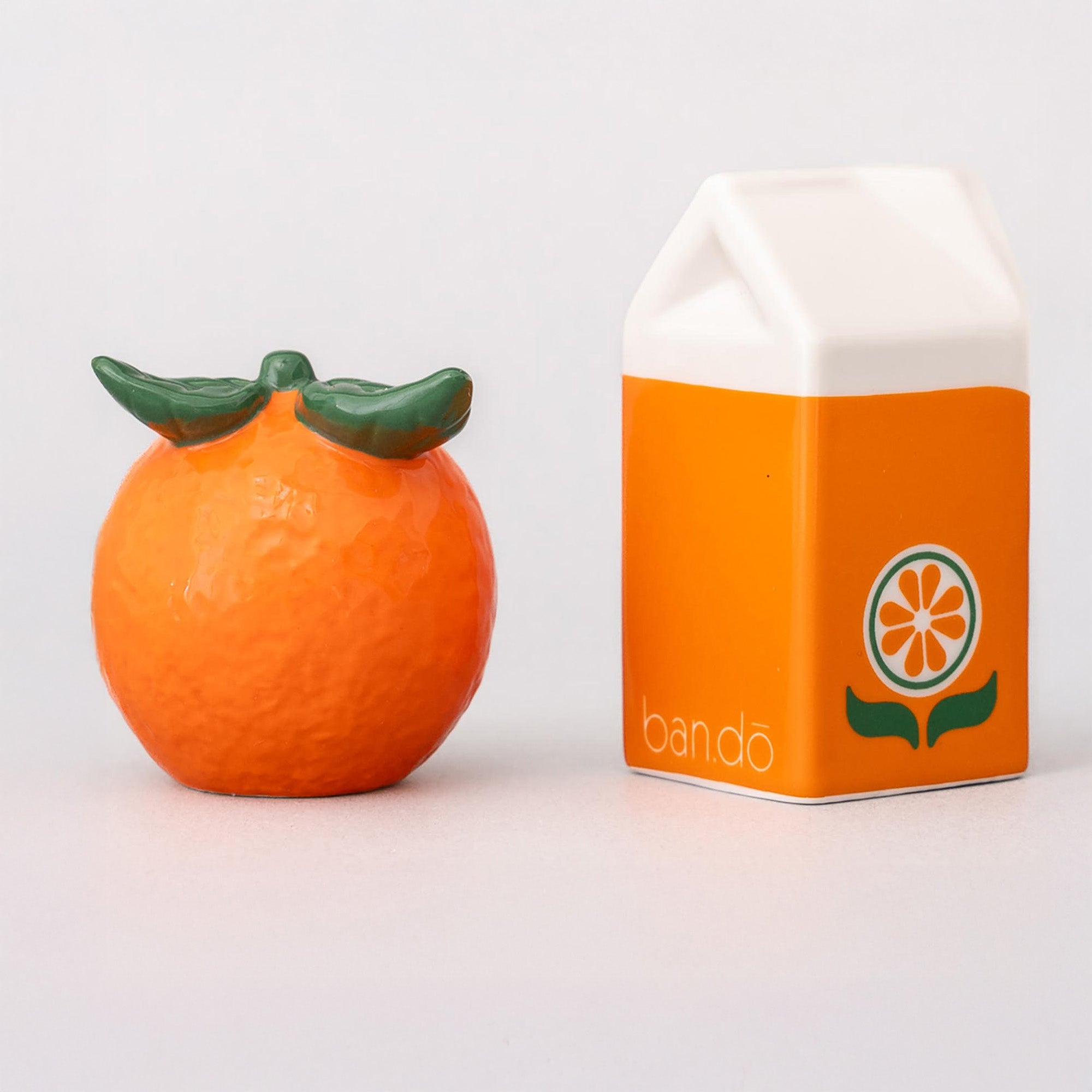Orange-shaped container with green top next to its packaging on a white background