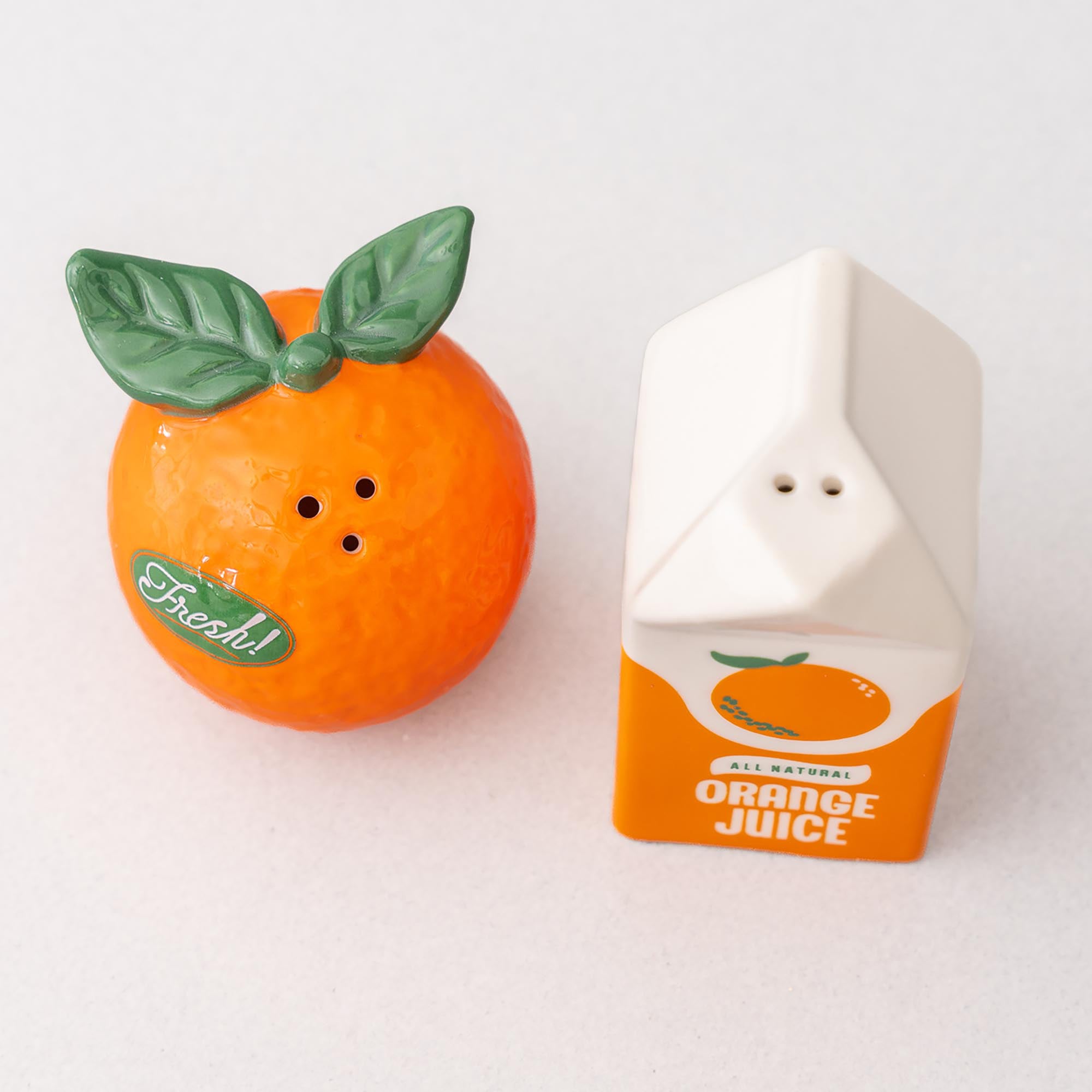Orange-shaped salt and pepper shaker with a carton-shaped orange juice container on a white background