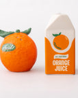 Decorative salt and pepper shaker shaped like oranges next to a box of all natural orange juice on a white background