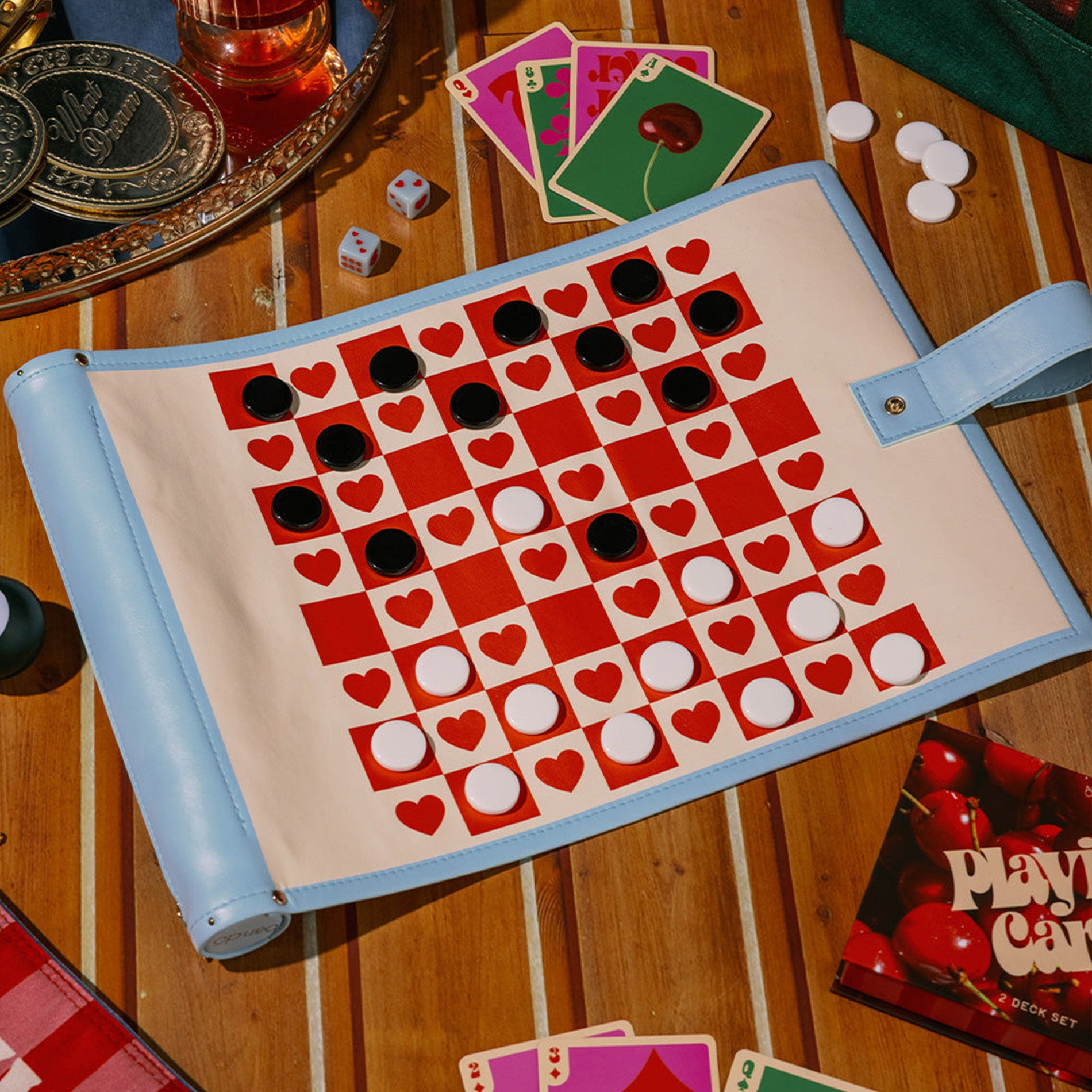 Checkers board with hearts on a wooden table with dice and cards.