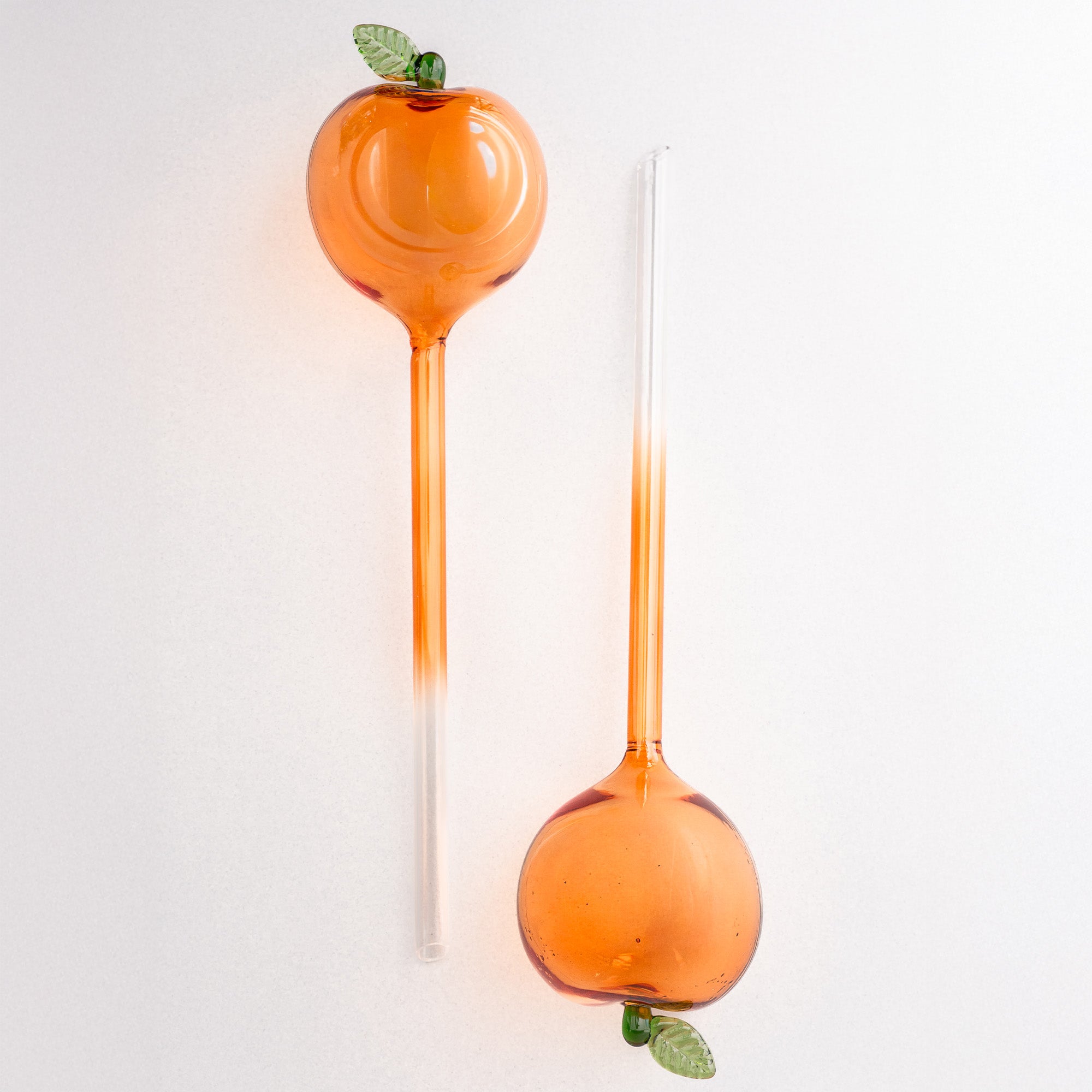 Two peach glass watering globes with green leaves on a white background
