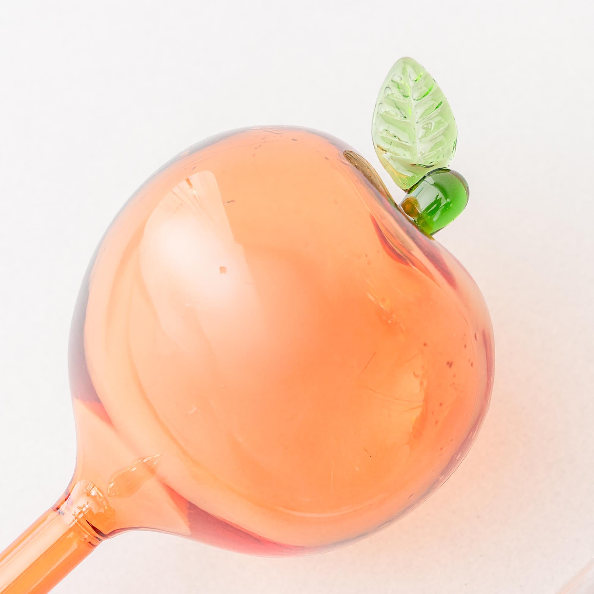 up close of Two peach glass watering globes with green leaves on a white background