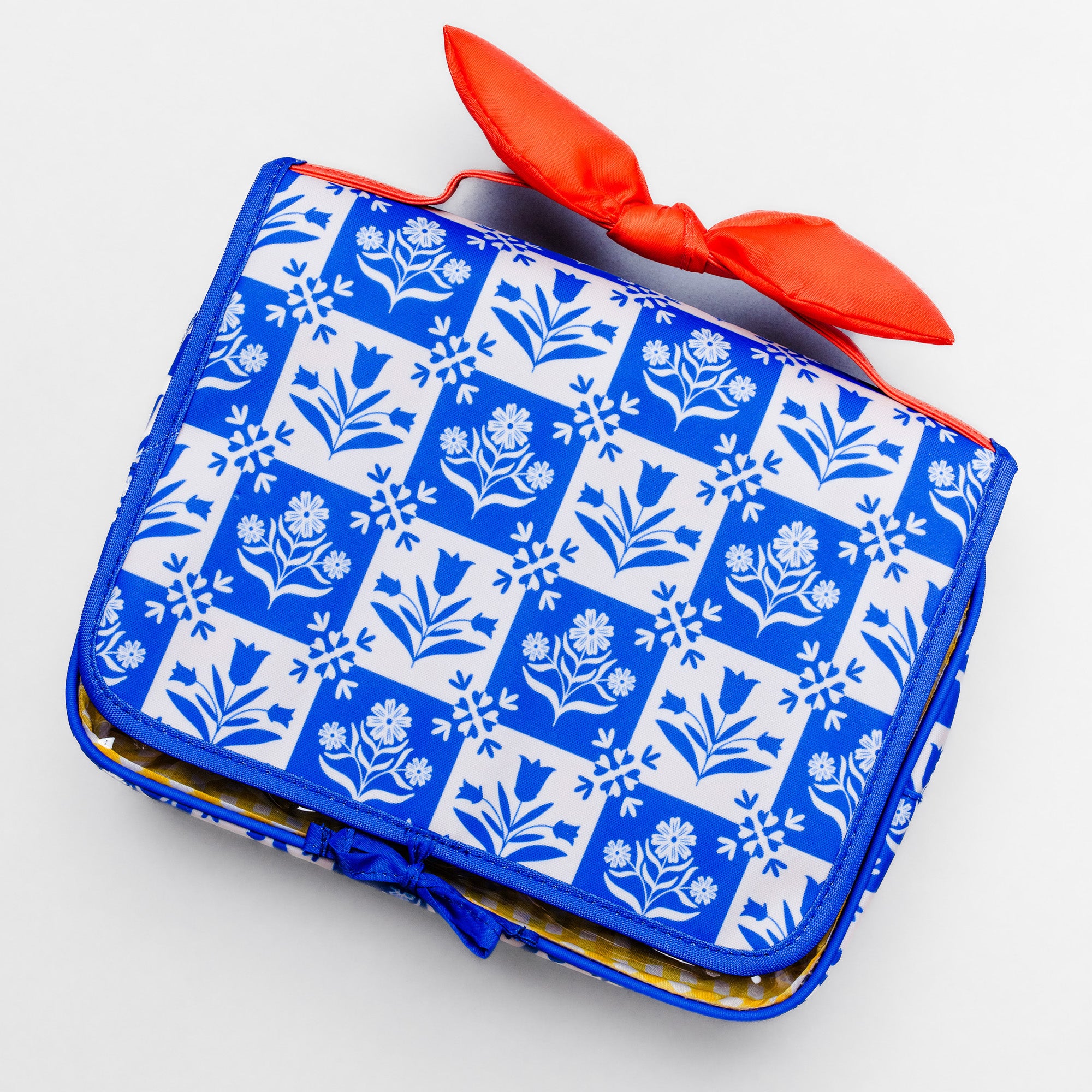 A blue and white patterned clutch bag with a bright red bow on top, photographed on a clean white background.