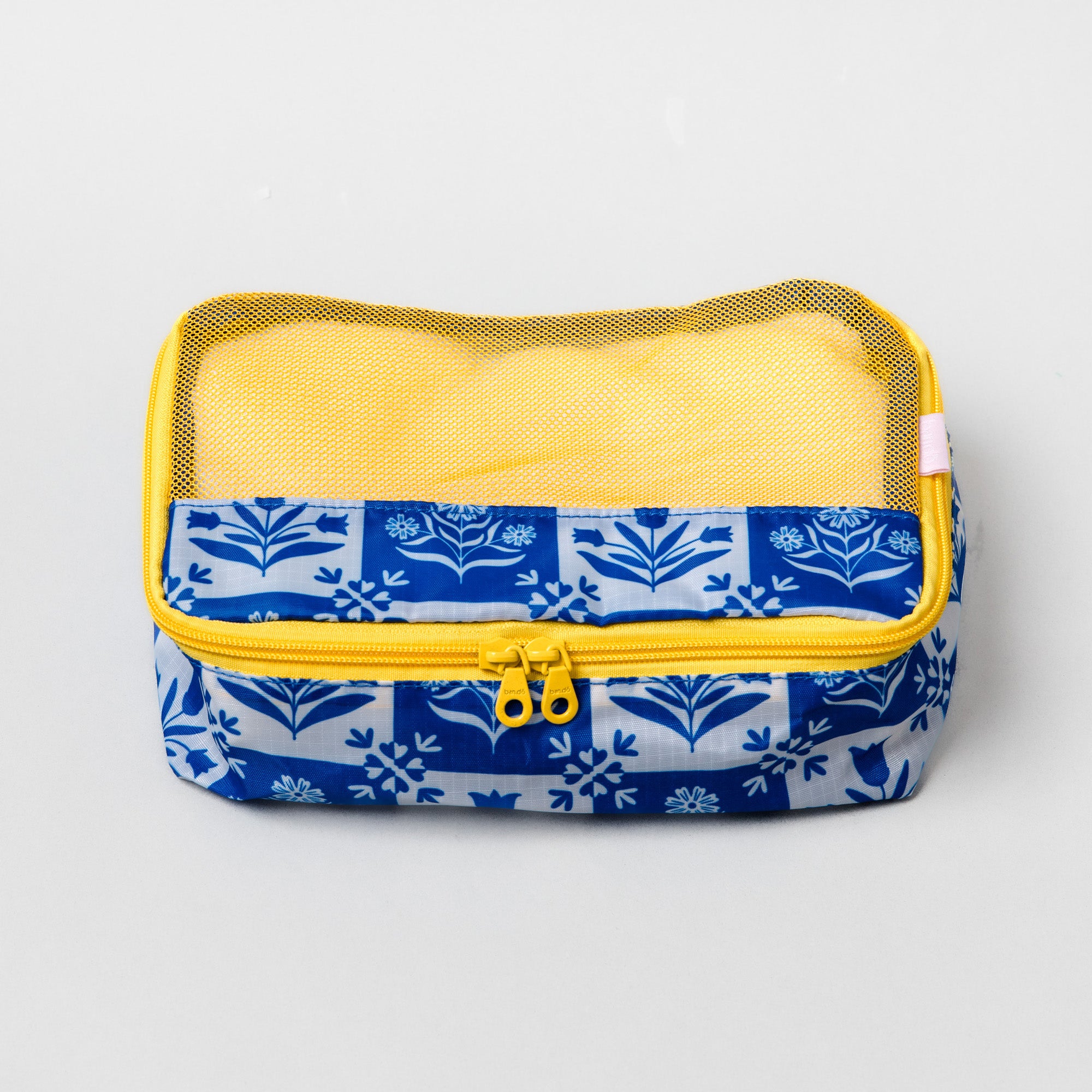 A rectangular mesh organizer pouch with a blue and white floral patterned fabric base, a yellow zipper, and a yellow mesh top, shown on a light gray background.