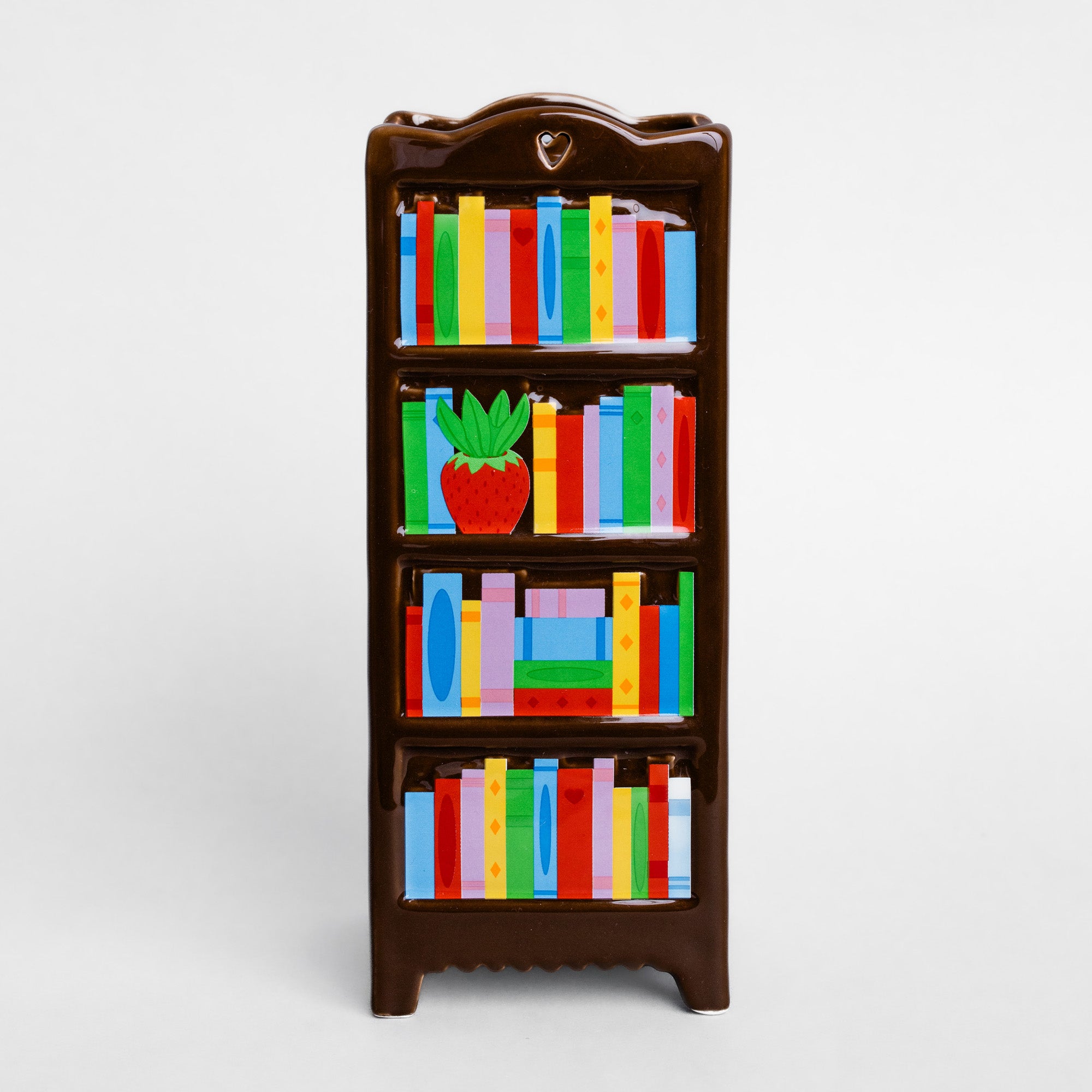 A small dark brown bookshelf vase decorated with colorful book spines and a red potted plant on the middle shelf, shown against a plain light gray background.