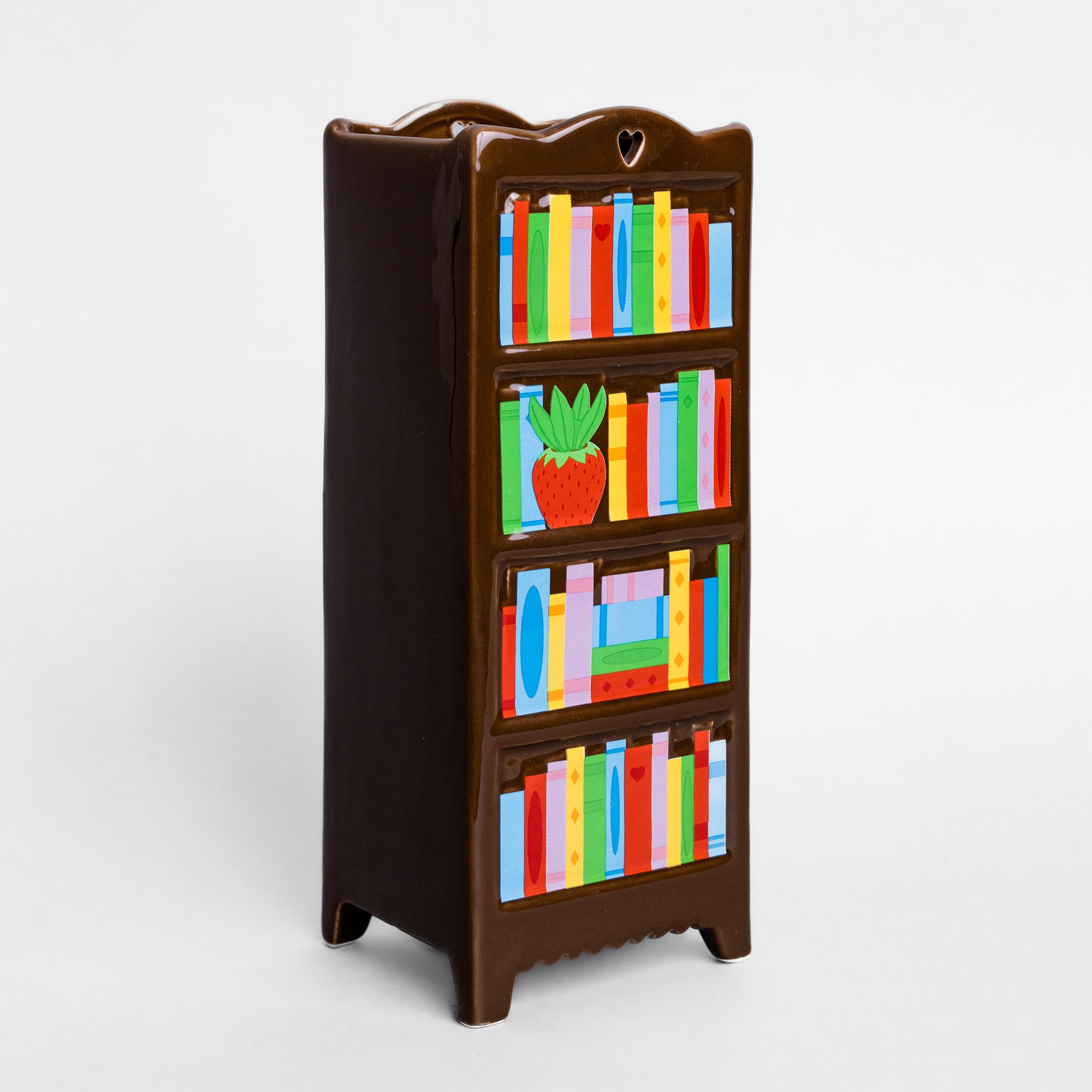 A dark brown wooden bookshelf with four shelves, decorated with colorful painted books and a small strawberry illustration, shown on a light gray background.
