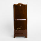 A glossy dark brown ceramic plant pot shaped like a miniature bookshelf featuring a small heart-shaped cutout at the top and a gold heart-and-arrow graphic with the word 'BOOMS' on the lower door, set against a plain light gray background.