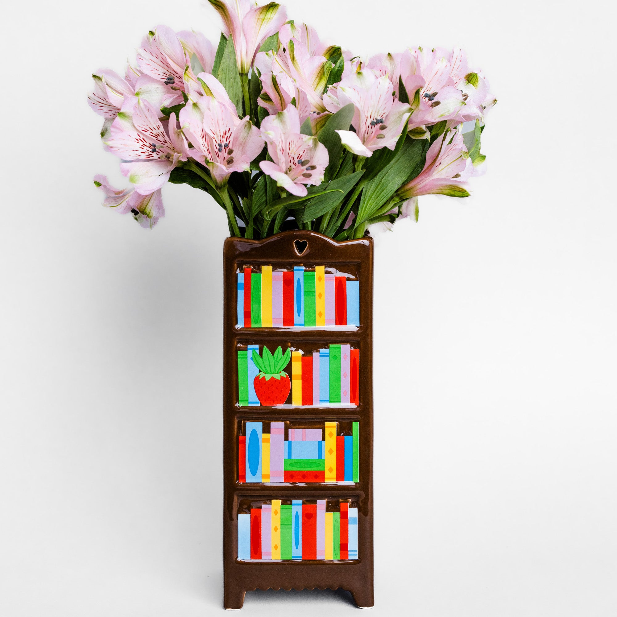 A brown bookshelf-shaped vase filled with pink alstroemeria flowers, set against a plain light gray background.