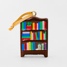 A small brown bookshelf-shaped ornament with colorful book spines and a yellow ribbon hanger, photographed on a clean light gray background.