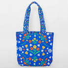A quilted blue tote bag with a colorful floral pattern, featuring green stems and leaves, orange and yellow flowers, and small white blossoms, set against a plain light gray background.