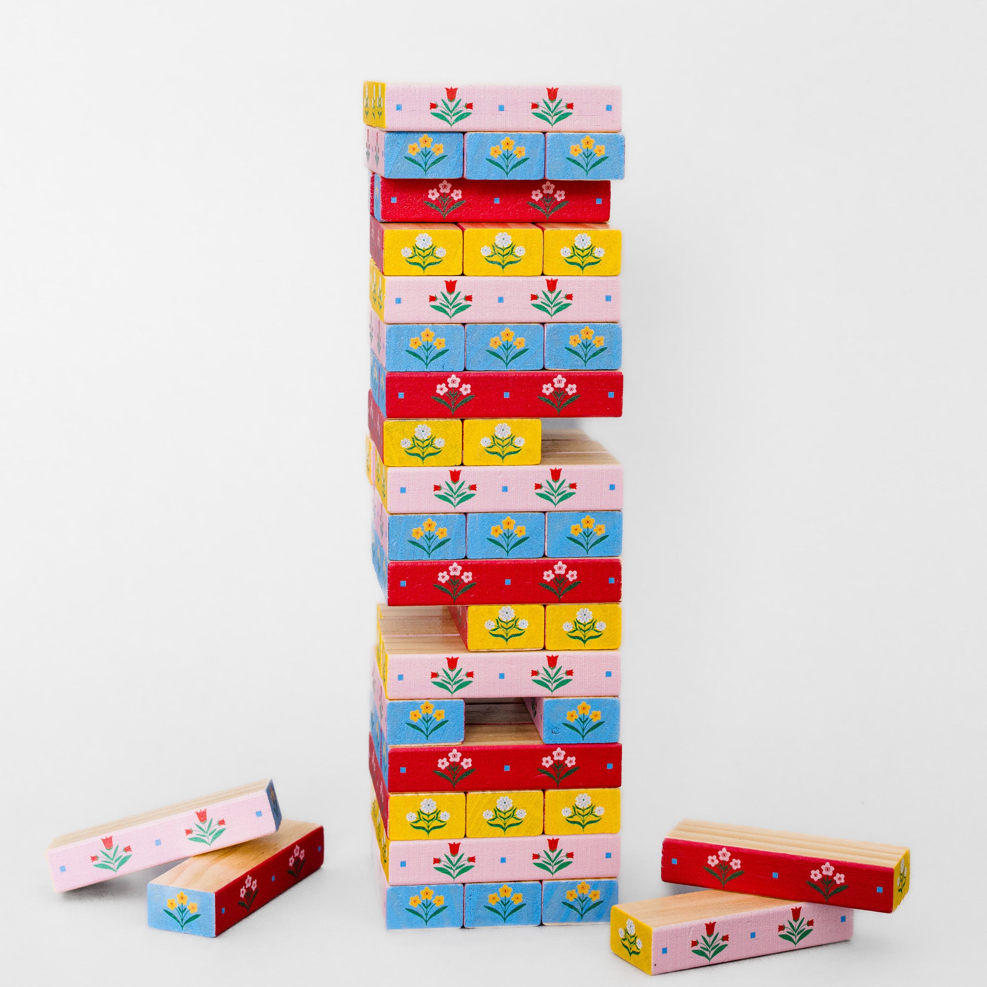 A colorful wooden block stacking game with rectangular blocks decorated with floral patterns in pink, blue, yellow, and red, arranged on a light gray background.
