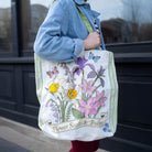 Person holding a tote bag with floral design and text 'Flower Seeds & Bulbs'.