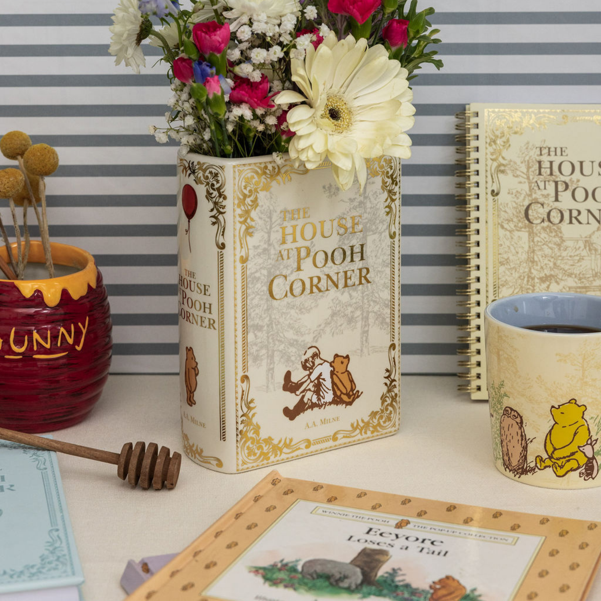Decorative items including a book-shaped vase with flowers, a mug, and a honey pot against a striped background.