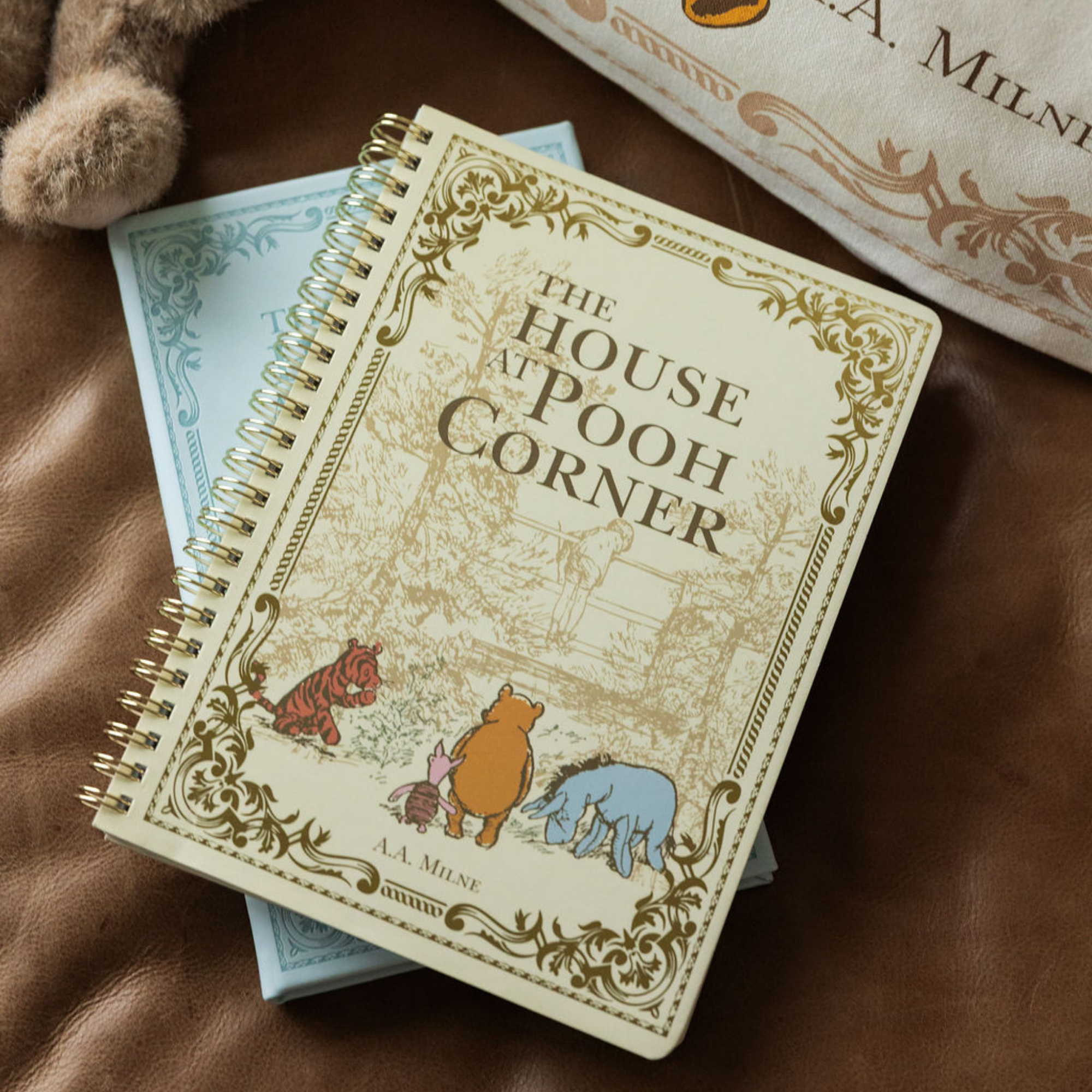 Notebook titled 'The House at Pooh Corner' by A.A. Milne on a brown surface with a teddy bear in the background.