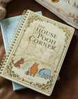 Notebook titled 'The House at Pooh Corner' by A.A. Milne on a brown surface with a teddy bear in the background.