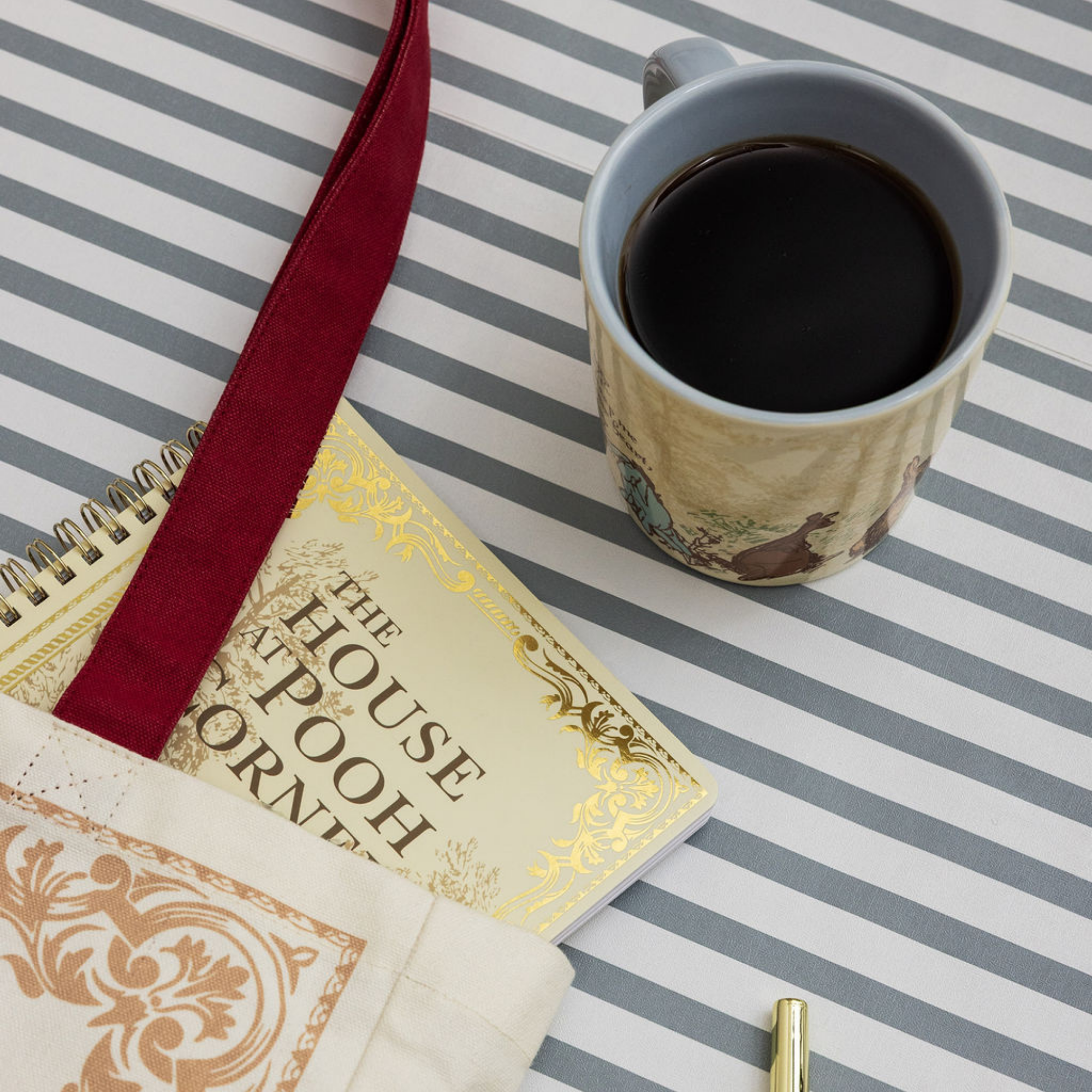 Cup of coffee next to a book titled 'The House at Pooh Corner' on a striped surface.