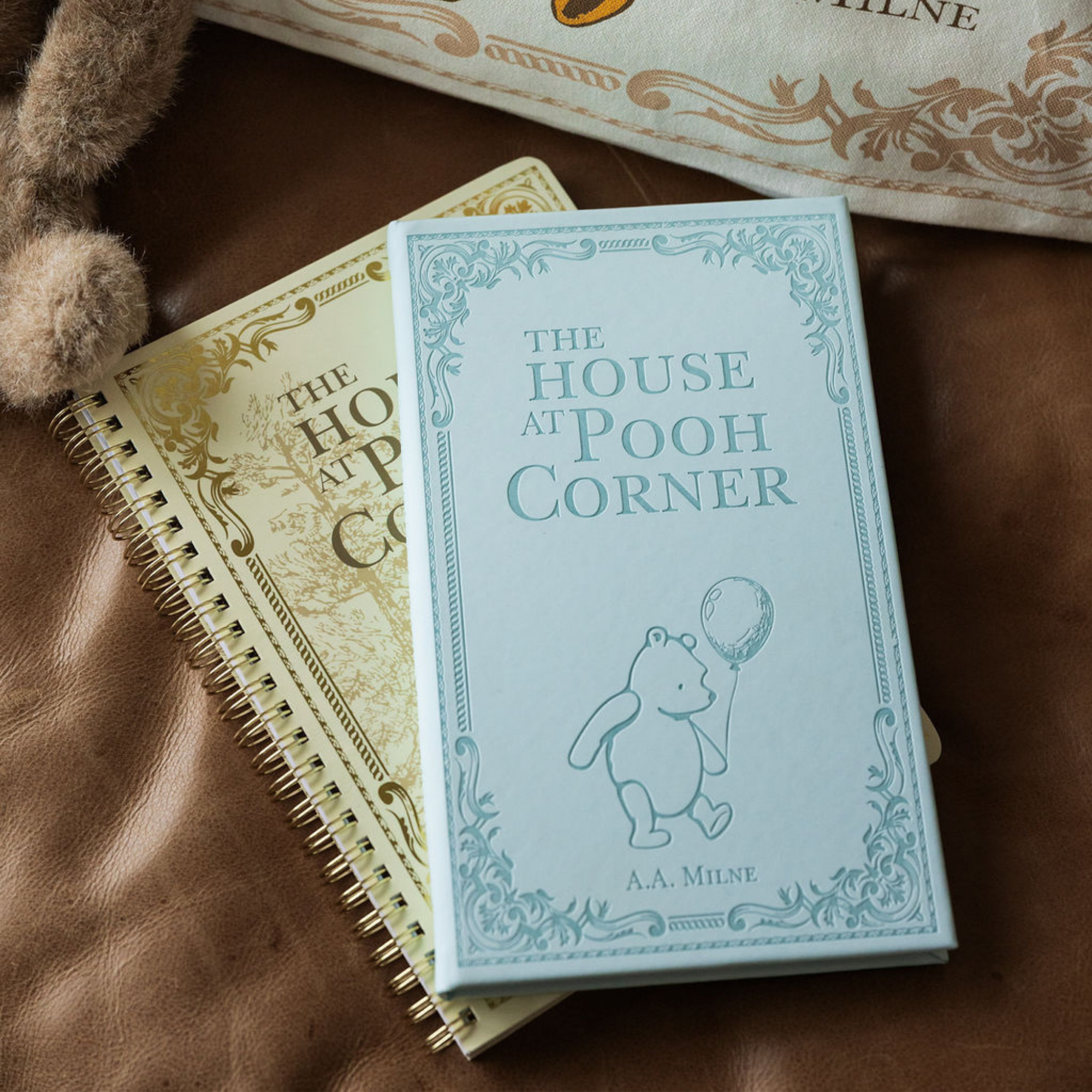 Book titled 'The House at Pooh Corner' by A.A. Milne on a textured surface with a teddy bear and another book.
