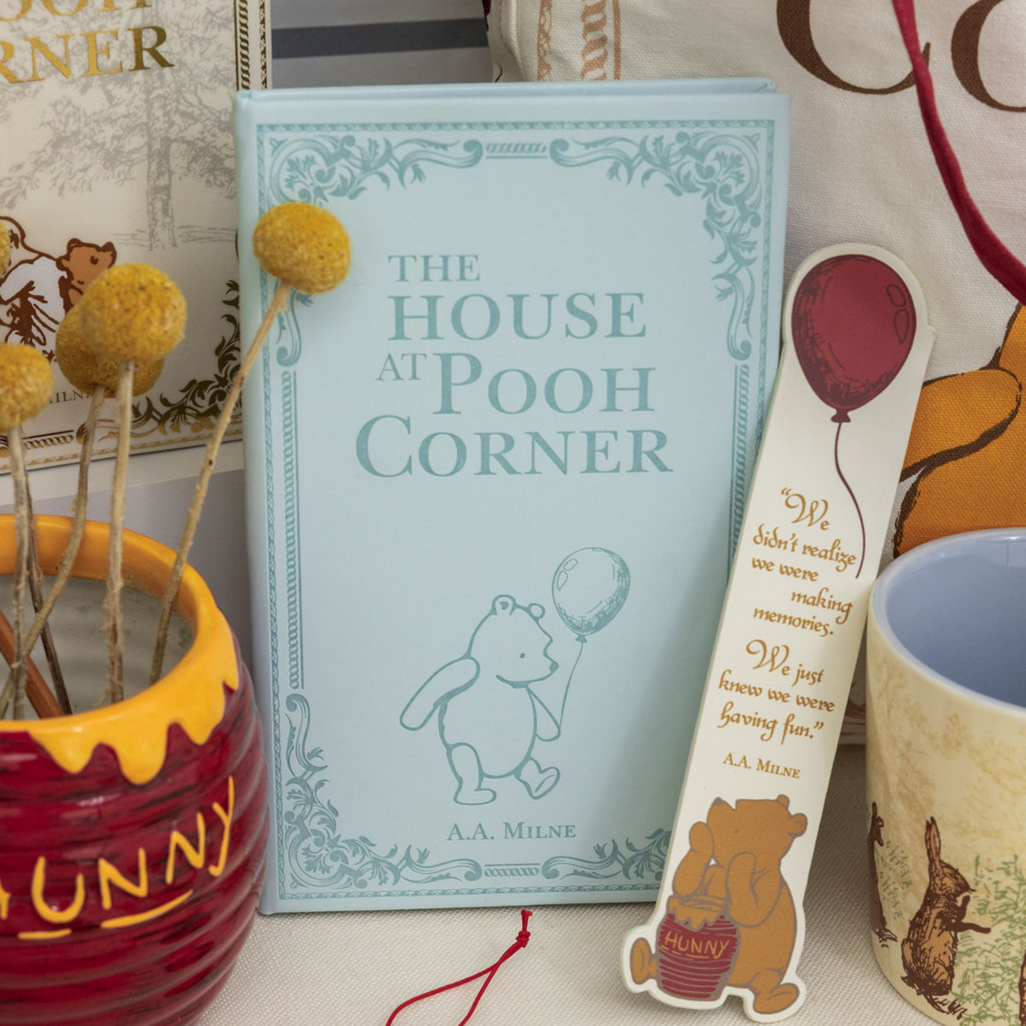 Book titled 'The House at Pooh Corner' with a bookmark featuring a bear and text, surrounded by decorative items.