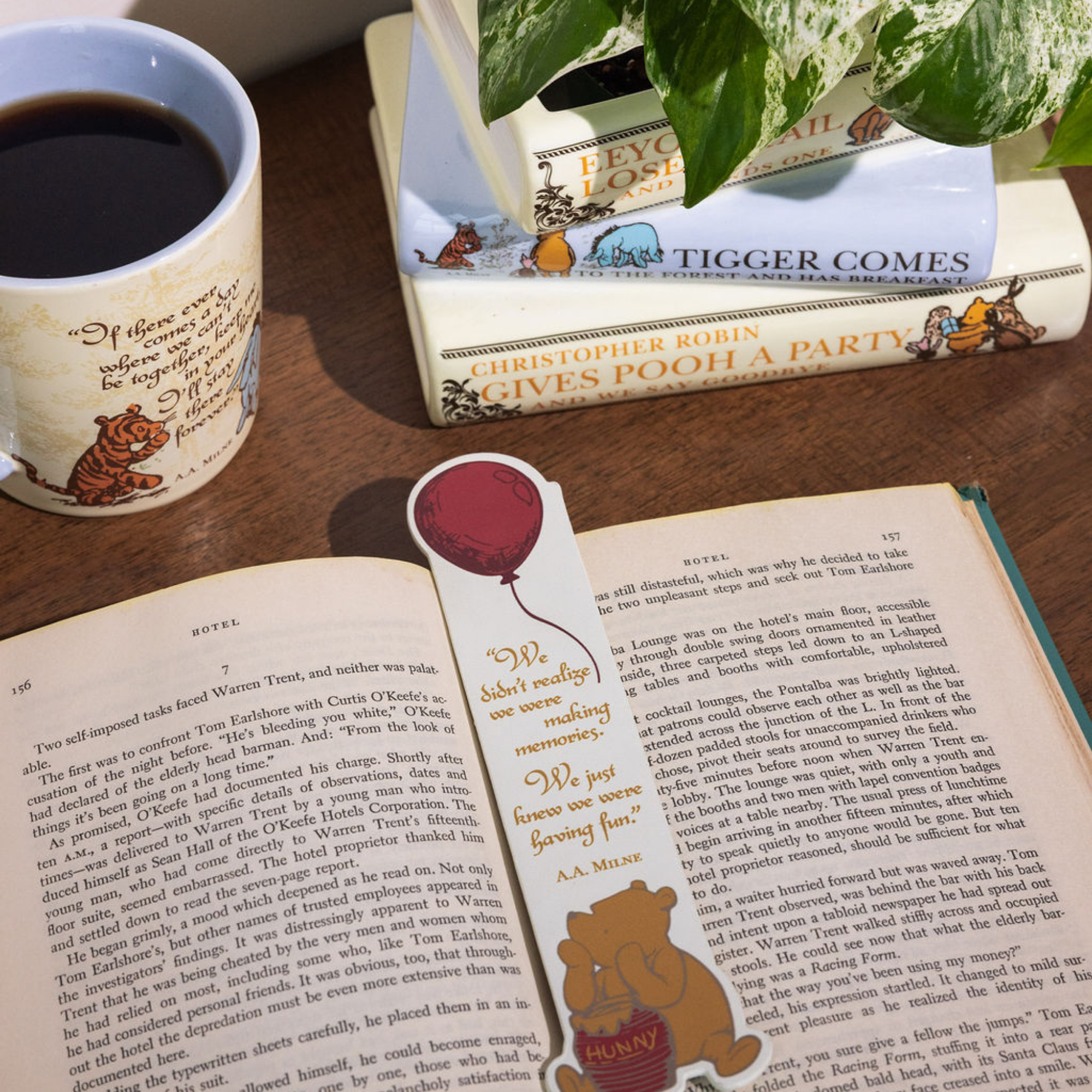 Open book with a bookmark featuring a bear holding a balloon, next to a mug with a bear design on a wooden surface.