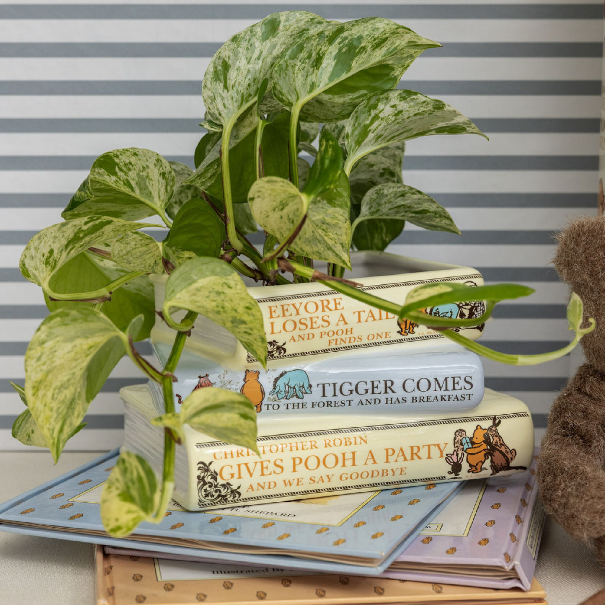 Stack of children's books with a plant and teddy bear on a striped background