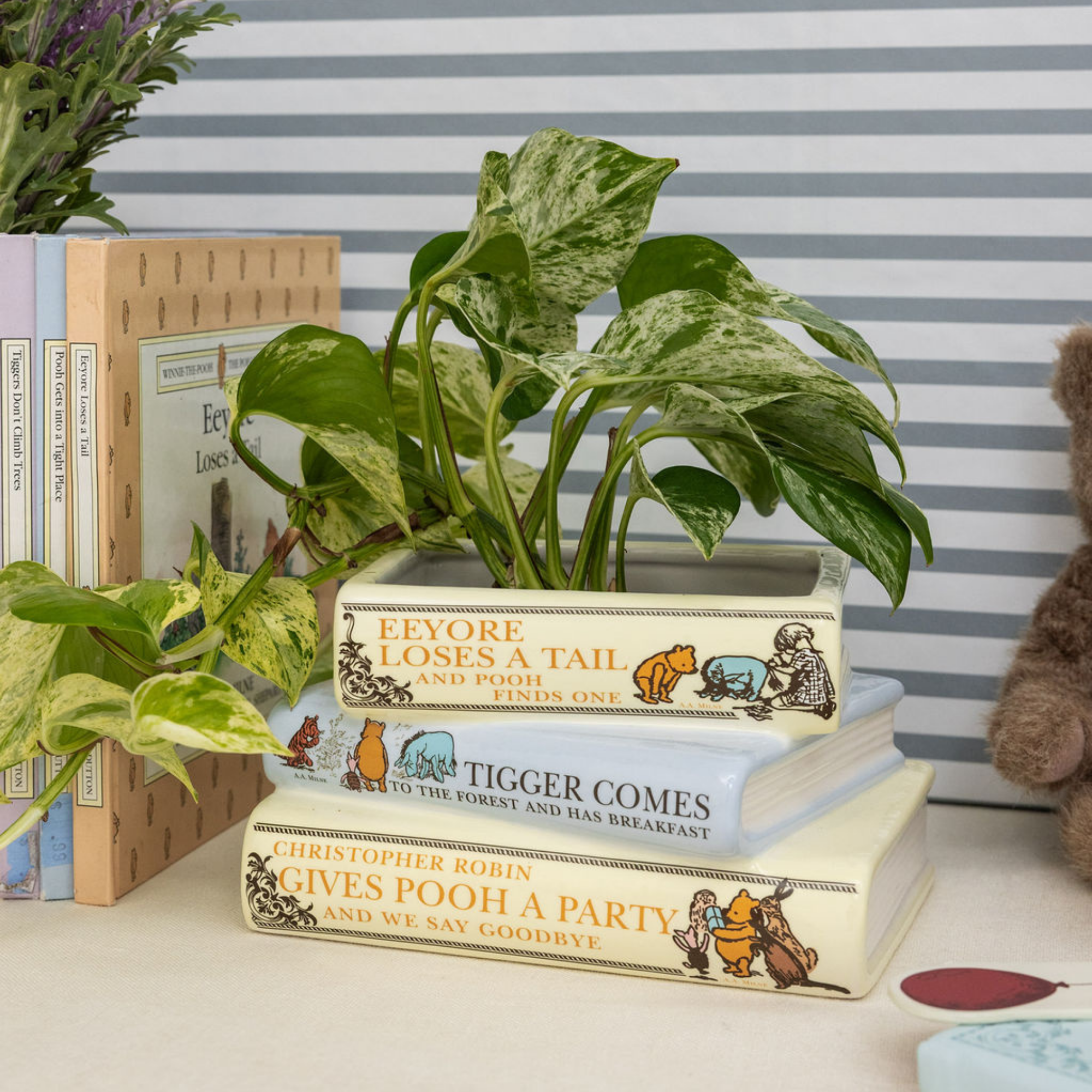 Decorative planter made from stacked Winnie the Pooh books with a plant inside, against a striped wall.