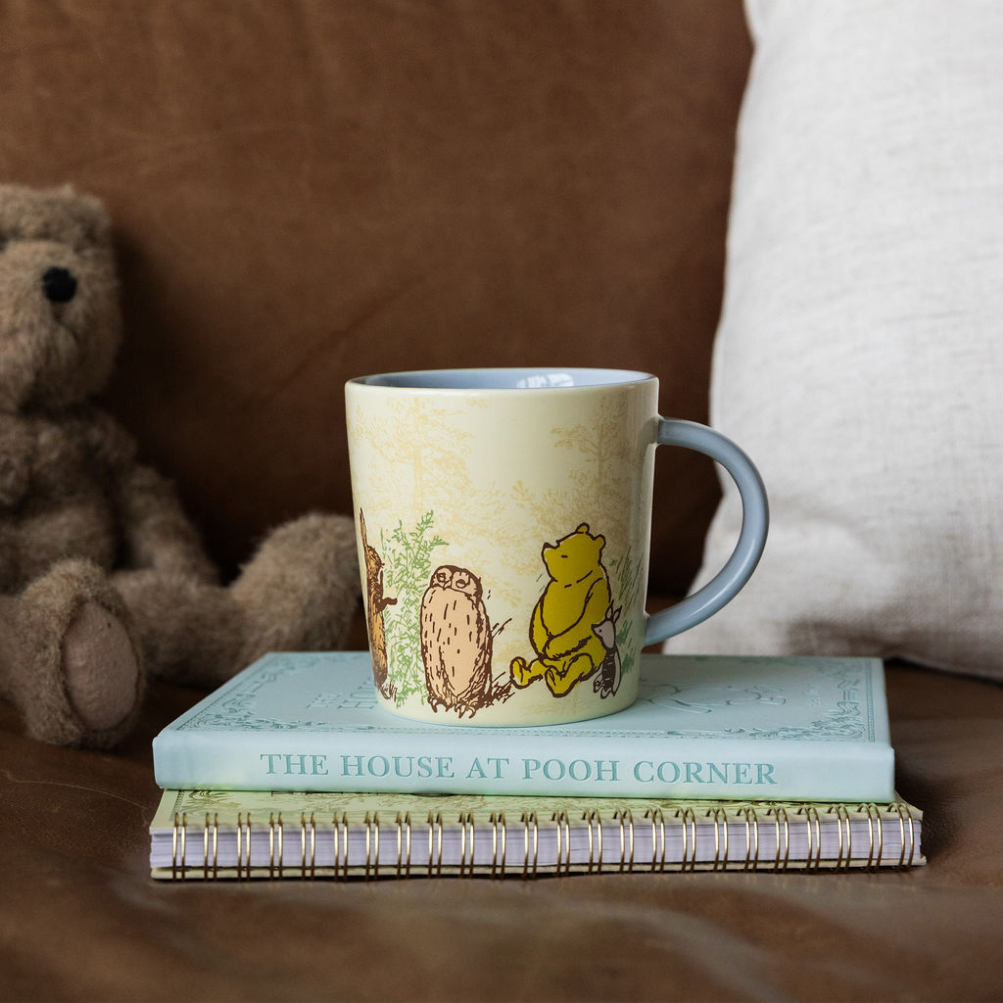 Mug with Winnie the Pooh design on a stack of books with a teddy bear in the background