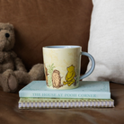 Mug with Winnie the Pooh design on a stack of books with a teddy bear in the background