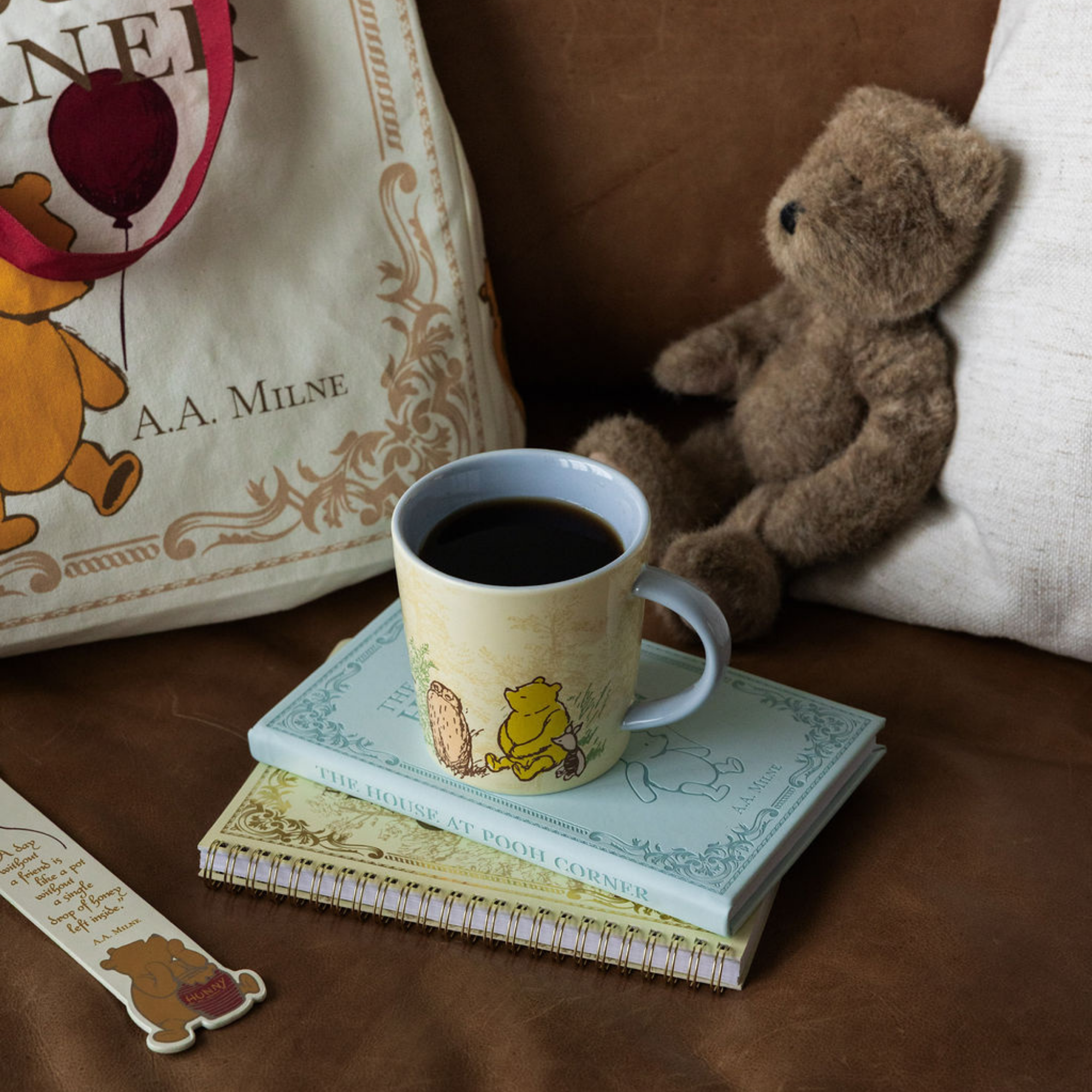 Cup of coffee with a teddy bear and books on a wooden surface, featuring A.A. Milne's 'Winnie the Pooh' books.