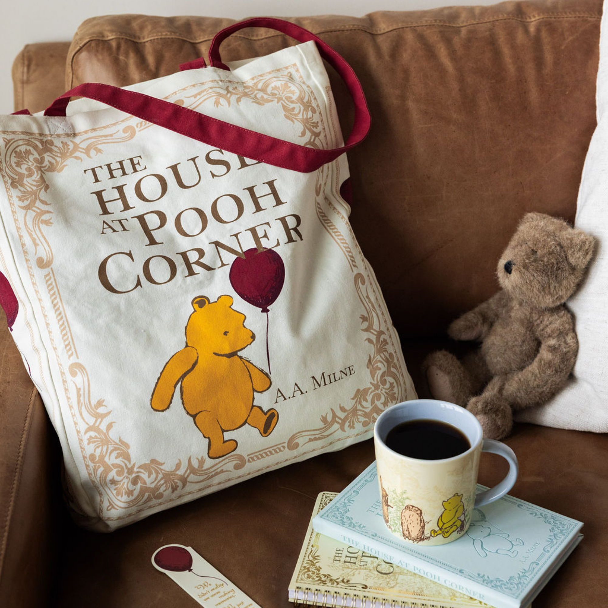 Tote bag with Winnie the Pooh design on a couch with a cup of coffee and teddy bear.
