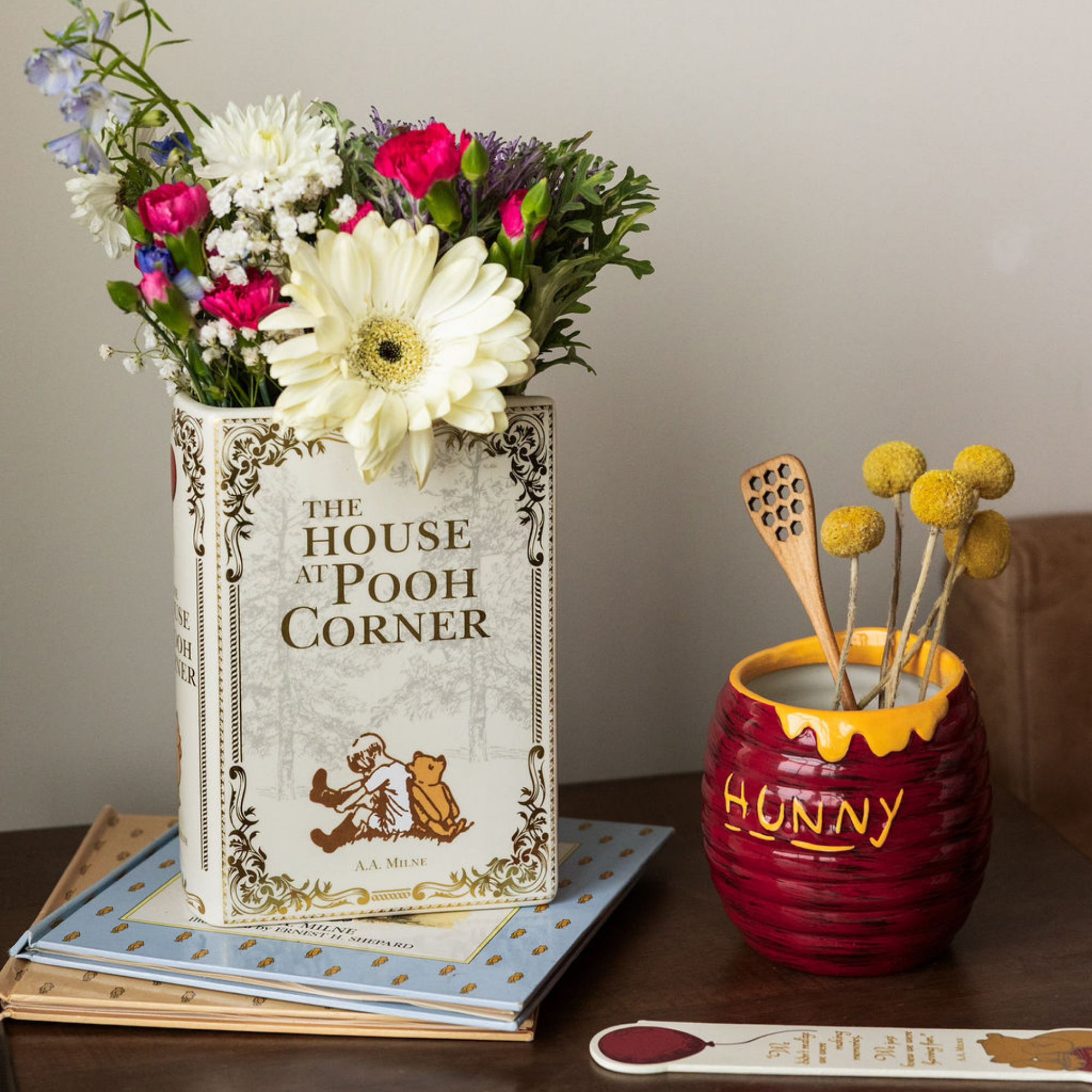 Decorative setup with 'The House at Pooh Corner' book, flowers, and a 'Hunny' pot on a table.