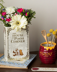 Decorative setup with 'The House at Pooh Corner' book, flowers, and a 'Hunny' pot on a table.