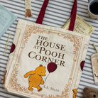 Book titled 'The House at Pooh Corner' with a bear illustration on a striped surface.