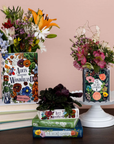 Floral arrangements in books with 'Alice's Adventures in Wonderland' and 'The Secret Garden' covers on a wooden surface.