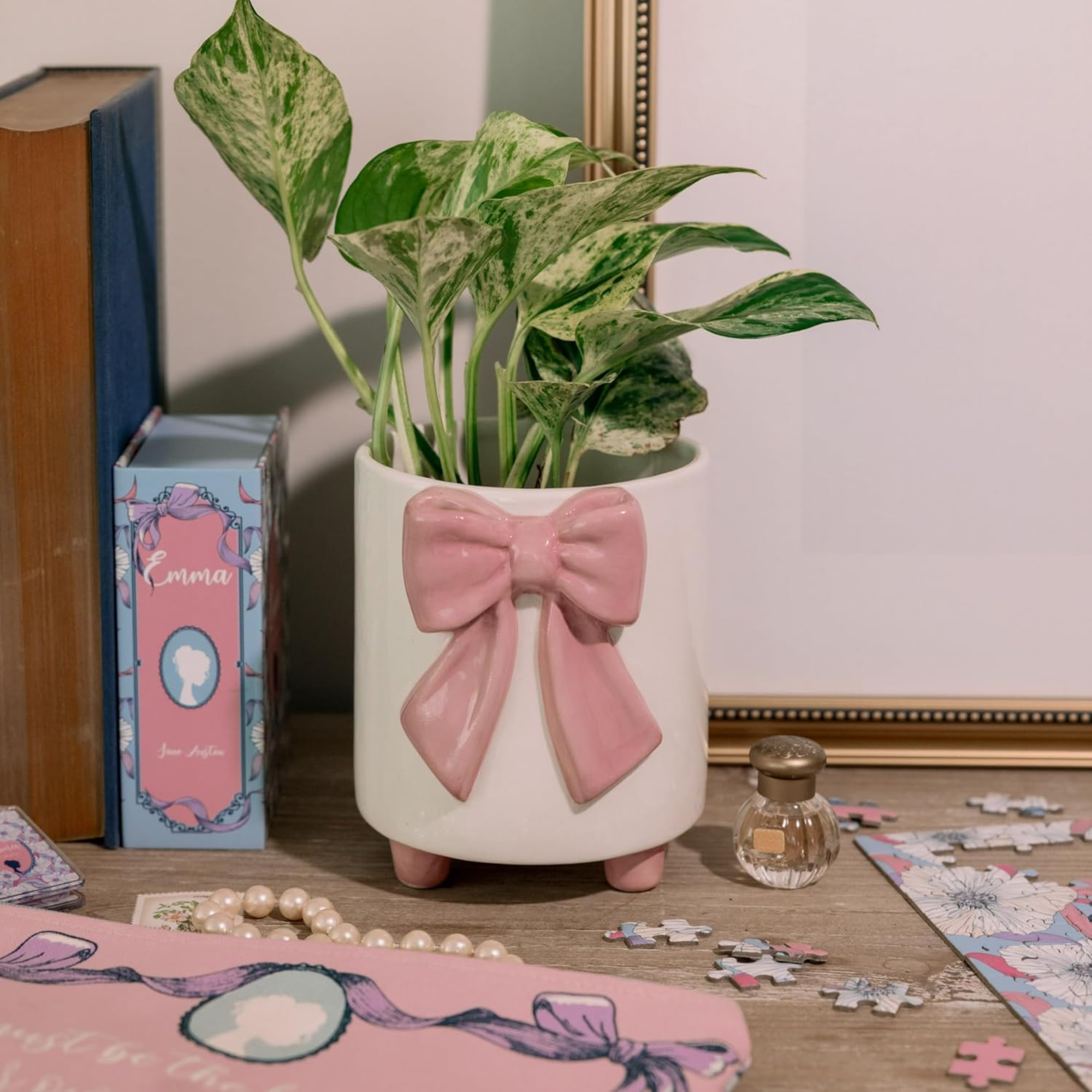 Decorative plant pot with a pink bow on a table with books and a puzzle.