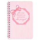 Pink notebook with decorative bow and text on a white background