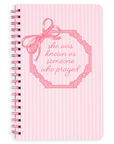 Pink notebook with decorative bow and text on a white background