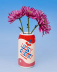 Red and white can-shaped vase with 'Lucky Cherry' branding holding pink flowers against a blue background