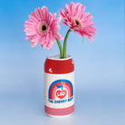 Red can-shaped vase with pink flowers against a blue background