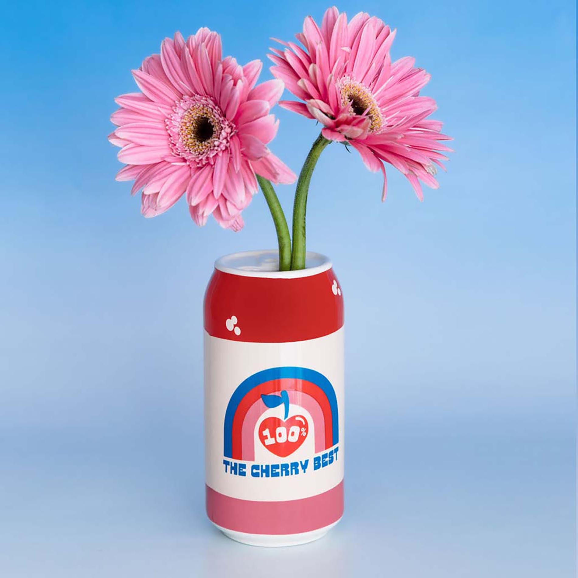 Red can-shaped vase with pink flowers against a blue background