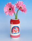 Red can-shaped vase with pink flowers against a blue background