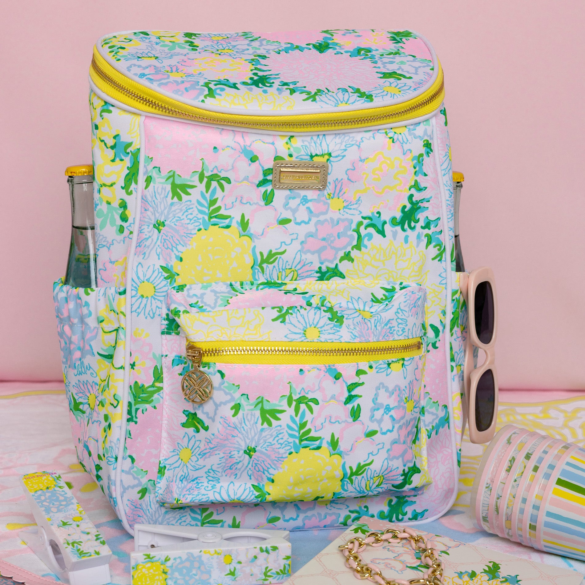 Floral-patterned cooler bag with sunglasses and a bottle on a pink background
