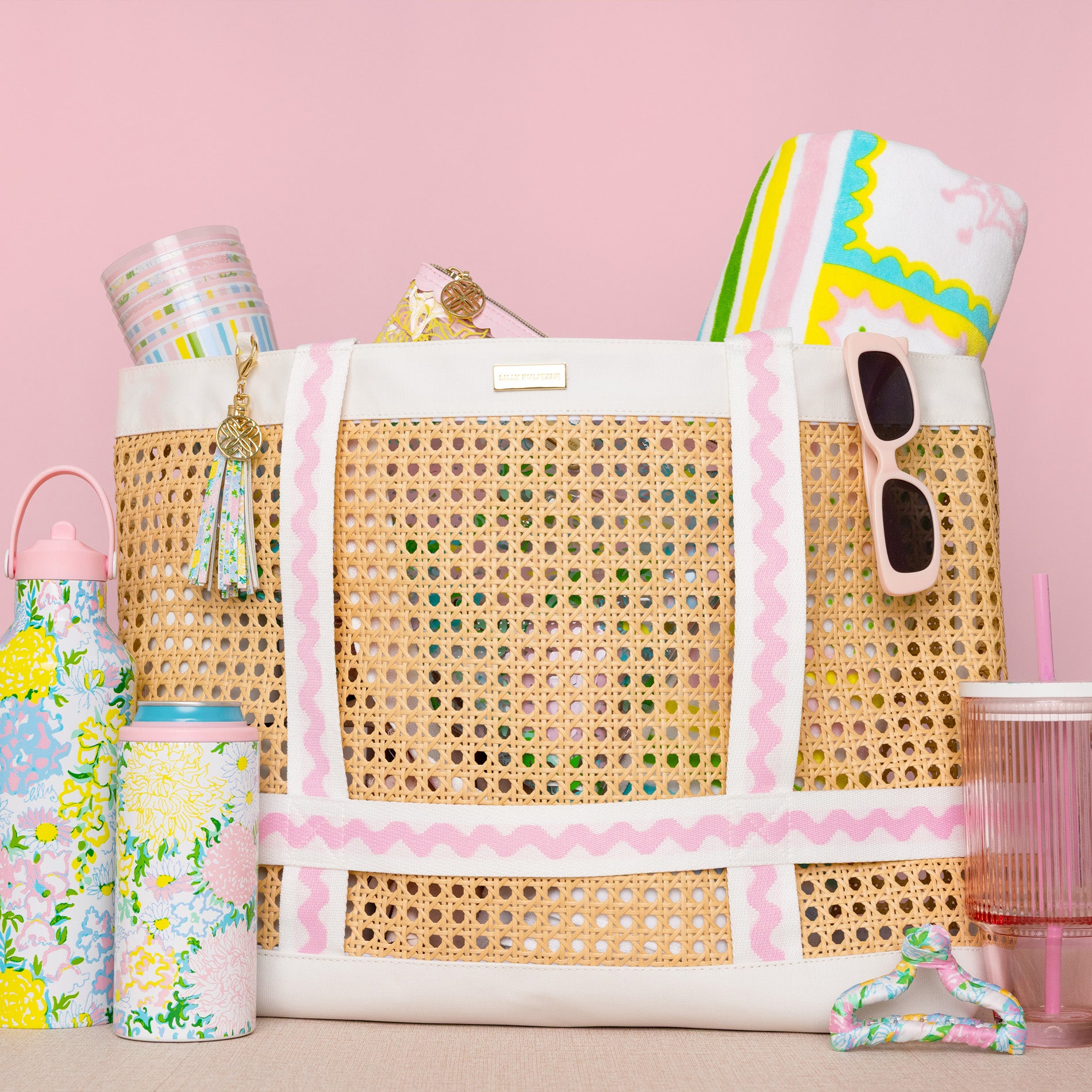 Woven tote bag with colorful accessories on a pink background