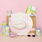 Collection of summer accessories including a hat, sunglasses, and water bottles on a pink background