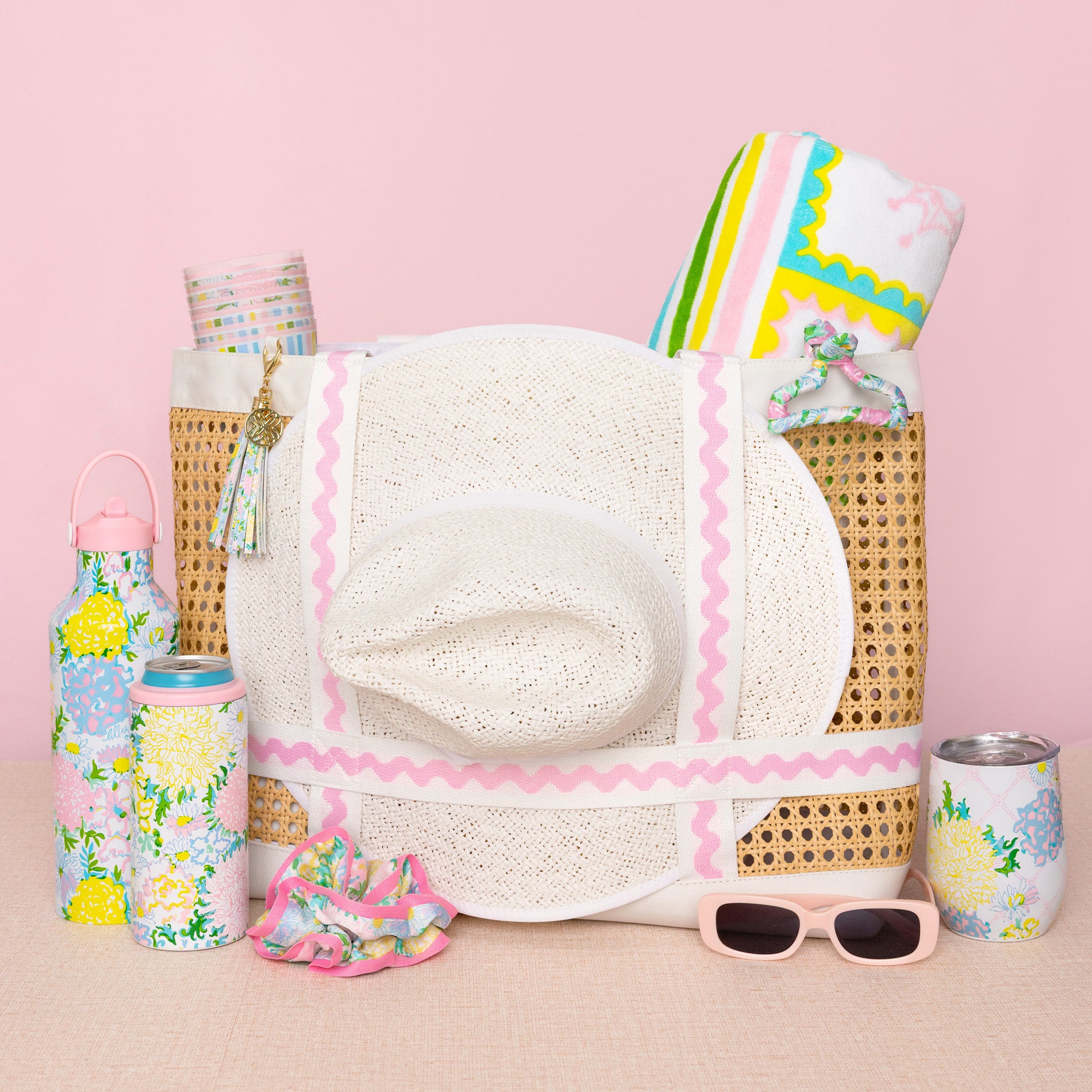 Collection of summer accessories including a hat, sunglasses, and water bottles on a pink background