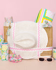 Collection of summer accessories including a hat, sunglasses, and water bottles on a pink background
